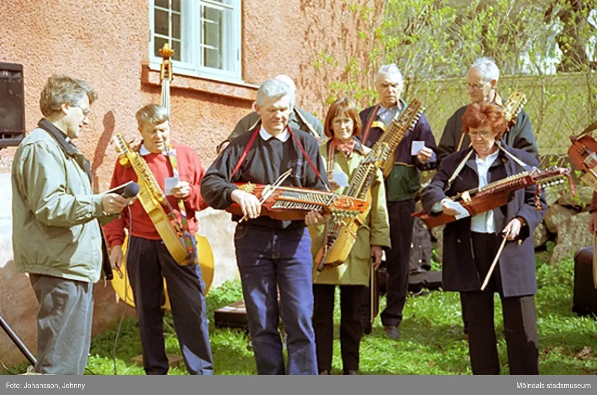 Kvarnbydagen 28 april 2002. Stensjöns församling har friluftsgudstjänst i Kvarnbyparken. 
I mitten står museitekniker Sven-Åke Svensson och spelar nyckelharpa i Lommebôs spelmansslag.