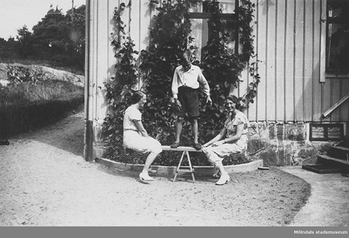 Sommar i Lindome i början av 1940-talet. Göte Hasselberg balanserar ståendes på en bräda. På var sida av brädan sitter två kvinnor. På höger sida Götes mor Anna Hasselberg, född Larsson. IBilden är troligtvis tagen i trädgården utanför Götes morföräldrars hem i Gastorp, Lindome.