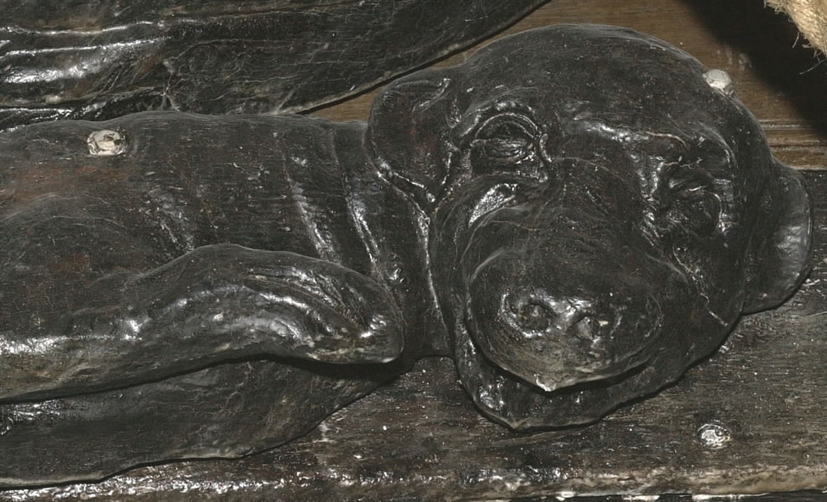 Skulptur av en säl, hund eller drake, återgiven i höger profil med det nedböjda huvudet riktat åt sidan.
Sälen har ett stort, trekantigt huvud med stora ögon och hängande öron. Foten är fenliknande. Den drakliknande stjärten fortsätter uppåt och avtecknar sig längs med stjärten till en triton, se fyndnummer 23079. Baksidan är slät.
Skulpturen är mycket välbevarad.

Text in English: A sculpture of a seal, dog or dragon carved in right profile with its bowed head turned to the side.
It has a large triangle shaped head with large eyes and hanging ears. Fin-like tail end. The dragon-like tail extends upwards onto a Triton situated above, see No. 23079.  The back is smooth.
The sculpture is very well preserved.