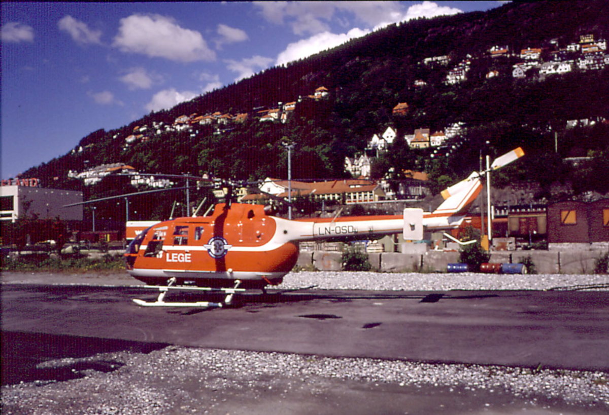 Lufthavn, ett ambulansehelikopte på bakken,  Eurocopter Deutschland HmbH BO 105S, LN-OSI fra Norsk Luftambulanse A/S. Bebyggelse i bakgrunnen.