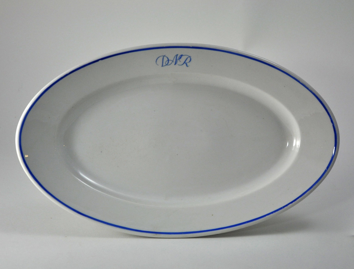 Ovalt fat i hvit porselen. A/S Den Norske Reiseeffektfabriks initialer "DNR" og munnigsrand påmalt i blått.