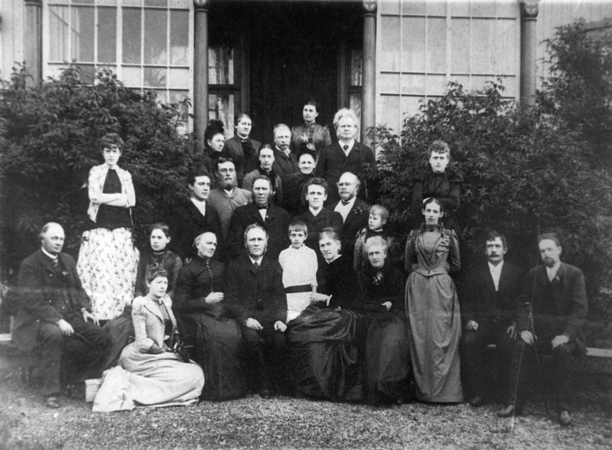 Gruppebilde av konfirmant med familie på trappen foran hus. Antatt tidlig 1900. Herren bakerst til høyre er antagelig Henrik Ibsen. Reprofotografi.