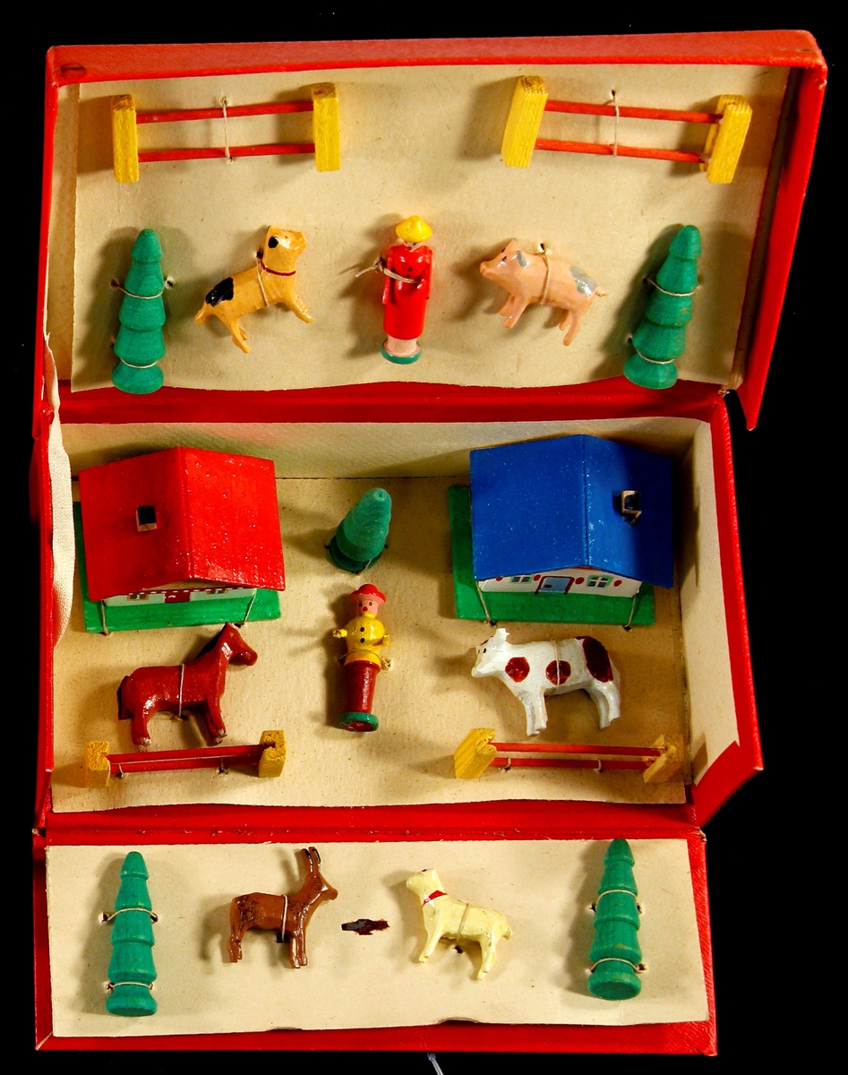 Små dyr, hus, dyr ,gjerder og trær  i miniatyr. Malt i friske farger. Ligger fastmontert i rød pappeske som kan brettes ut ved åpning. To hus, 6 dyr, 2 personer, 5 trær, 4 gjerder.