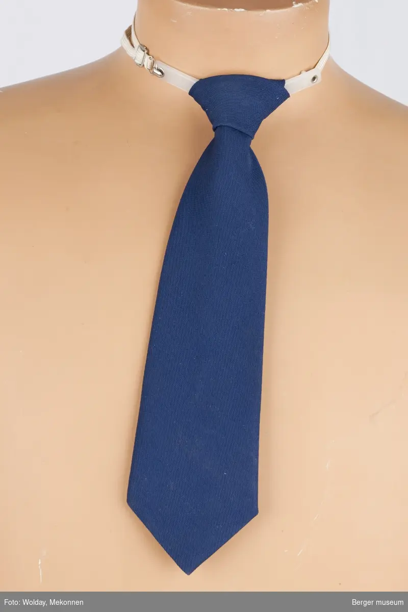 Slipset er enkelt blått. Det er knute på det og festes rundt halsen med strikk og en plastanordning.