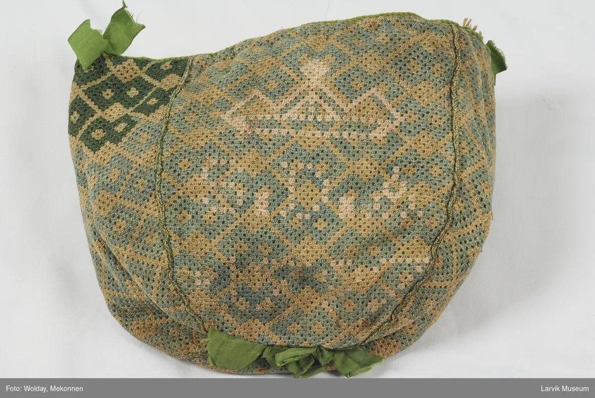 Form: Satt sammen av 4 kileformede stykker, kantet med grønn snor, foret med grønn silke, løpegang og sammentrekksnor øverst.sløyfer i silke.
