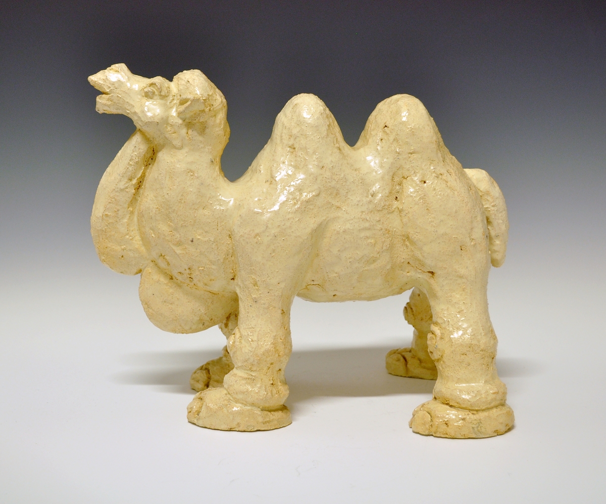 Figur av keramikk. Topuklet kamel, grovt modellert, nærmest "lyserødbeige" farge. Kunstner: Nora Gulbrandsen.