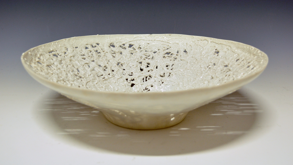 Fat i porselen. Fotrand, rund, buet form. Delvis, tilfeldig gjennombrutt. Porslensmasse tilfeldig sprøytet utover. Hvit glasur. Ustemplet.
Kunstner: Anne-Marie Ødegaard.