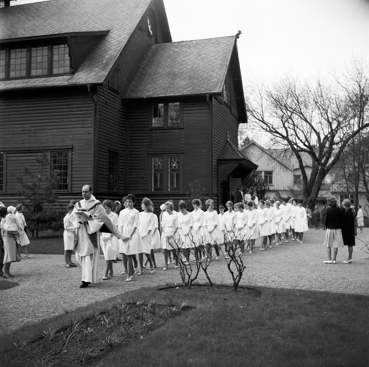 Konfirmation i Huskvarna kyrka. Flickorna är klädda i vita knälånga klänningar, vita skor och vita vantar.