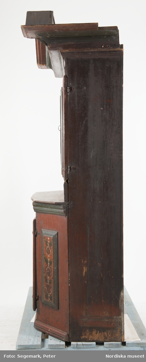 Med nyckel.

Katalogkort:
"Skåpets nedre del m. enkel dörr o lås; en hylla. Övre del med dubbeldörrar och lås med nyckel; en hylla, en skedhållare; två lådor närmast skänken nedanför dubbeldörrarna. På ena dubbeldörrens insida märkt: 1782
på utsidan: 1842 NES AOD
Färg mörkröd, grönt listverk; dekor ljusgul, grönblå, svart."
"1848. N.E.SA.O.D. övermål. ANNO 1788."