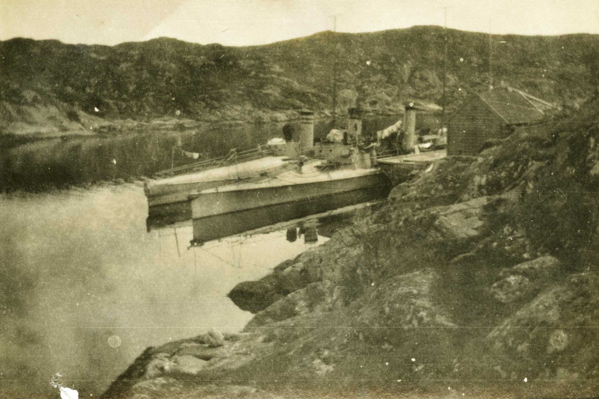 Krig - Småfartøy - Kystlandskap
I Bakkesund ved Korsfjorden august 1920.
t/b "Skrei" og "Teist". Torpedobåtene ligger til land på den nærmeste landsiden i en fjord. Båtene ligger med langsiden mot hverandre. Landskapet synes å være sterkt kupert.