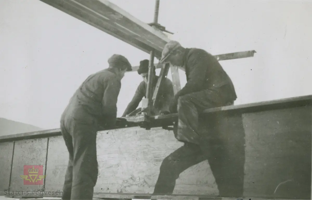 Vingnesbrua under oppbygging 18.12.1933. En bjelke transporteres ut for montering. Mennene på bildet er ukjente.