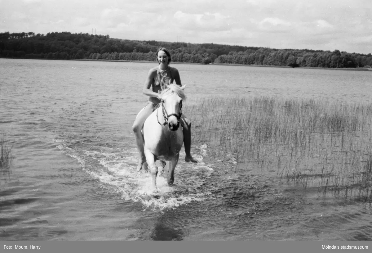 Flicka rider på häst vid en sjö, år 1983. 

"Ridtur i sommarland 
Sommar, sommar, sommar.
En härlig årstid för oss alla. Behovet av svalka är stort även hos våra fyrbenta vänner. Här är det Jorunn som ser till att hennes häst Teddy får svalka."

Fotografi taget av Harry Moum, HUM, för publicering i Mölndals-Posten, vecka 29, år 1983.