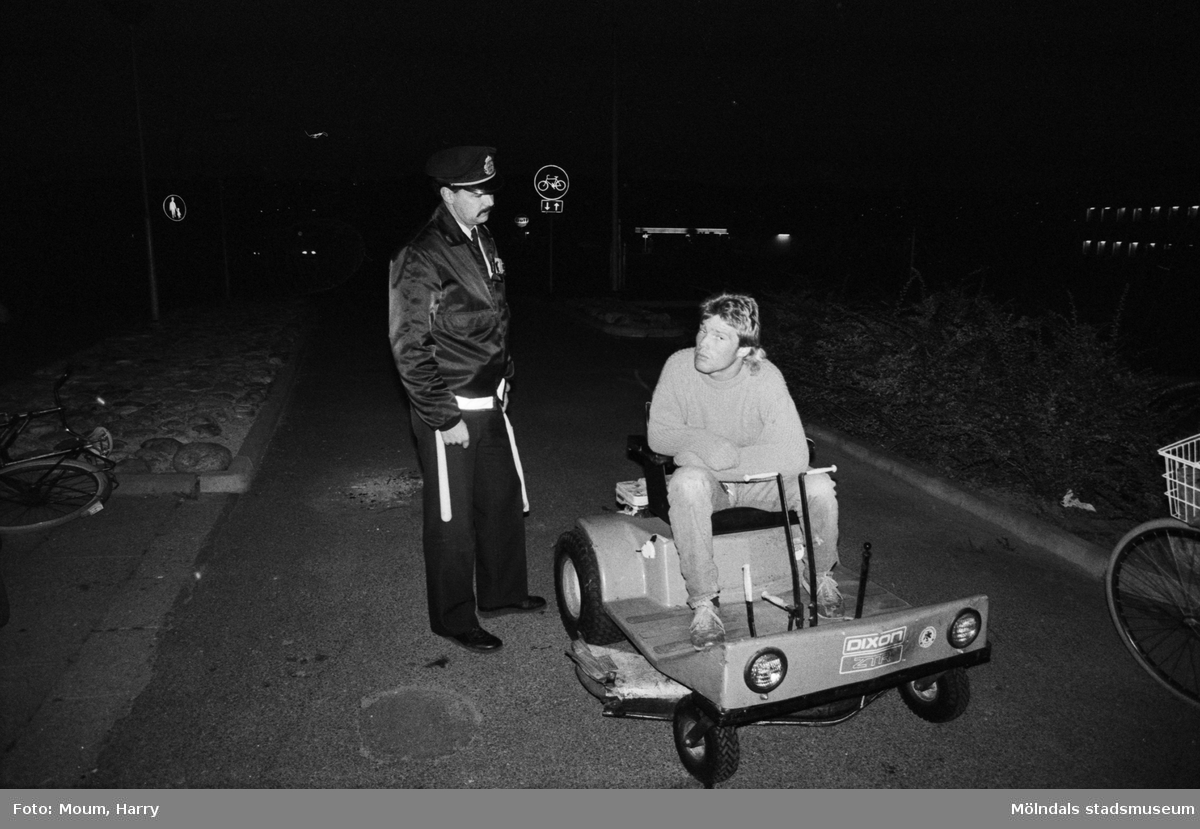 Kvarterspolis Ola Candefors, Batong-Ola kallad, ses tillsammans med en pojke som sitter på något slags fordon utanför Almåsgården i Lindome, år 1983.

För mer information om bilden se under tilläggsinformation.