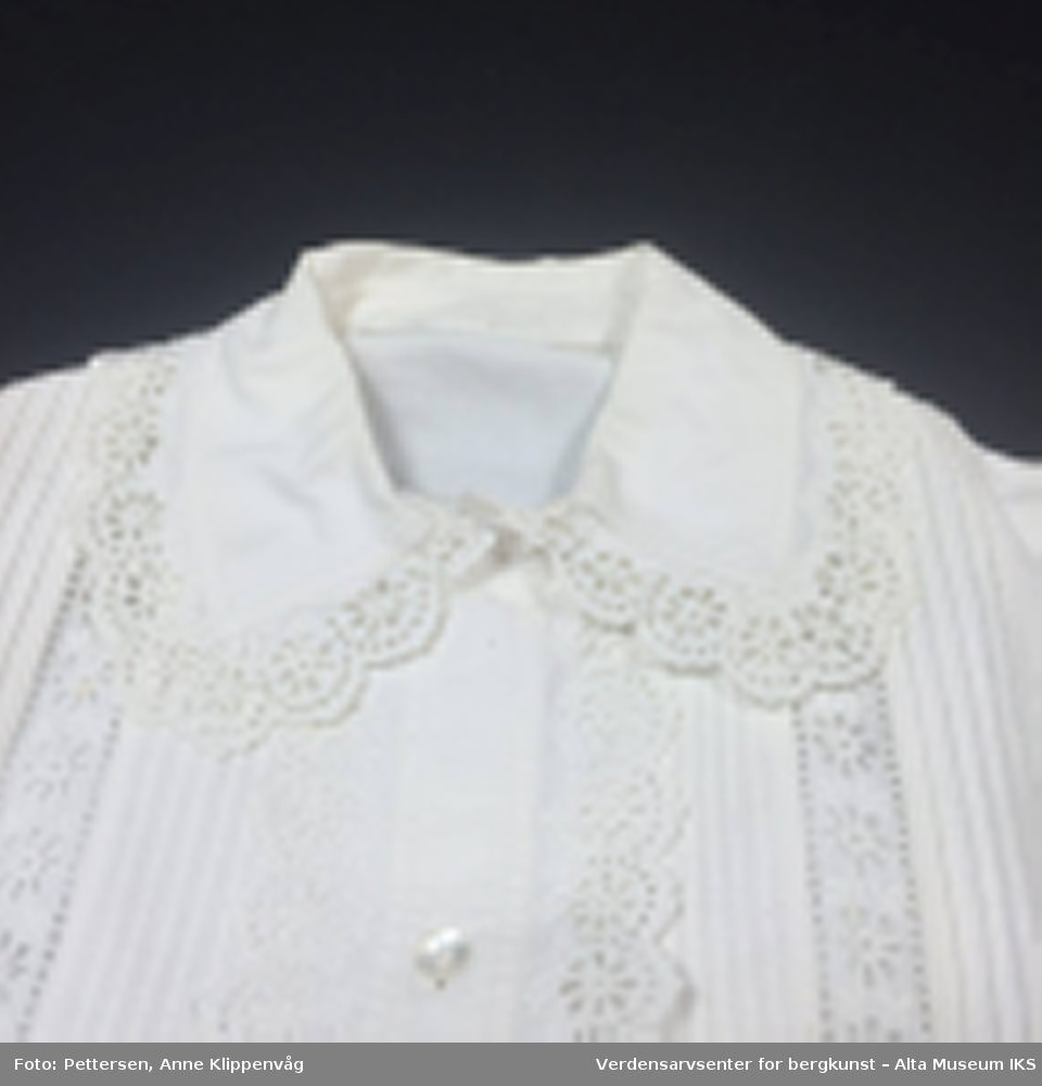 Langermet hvit skjorte med blonder rundt ermer, krage og ned langs forsiden.  Forknappet kvinneplagg med biser og blonder