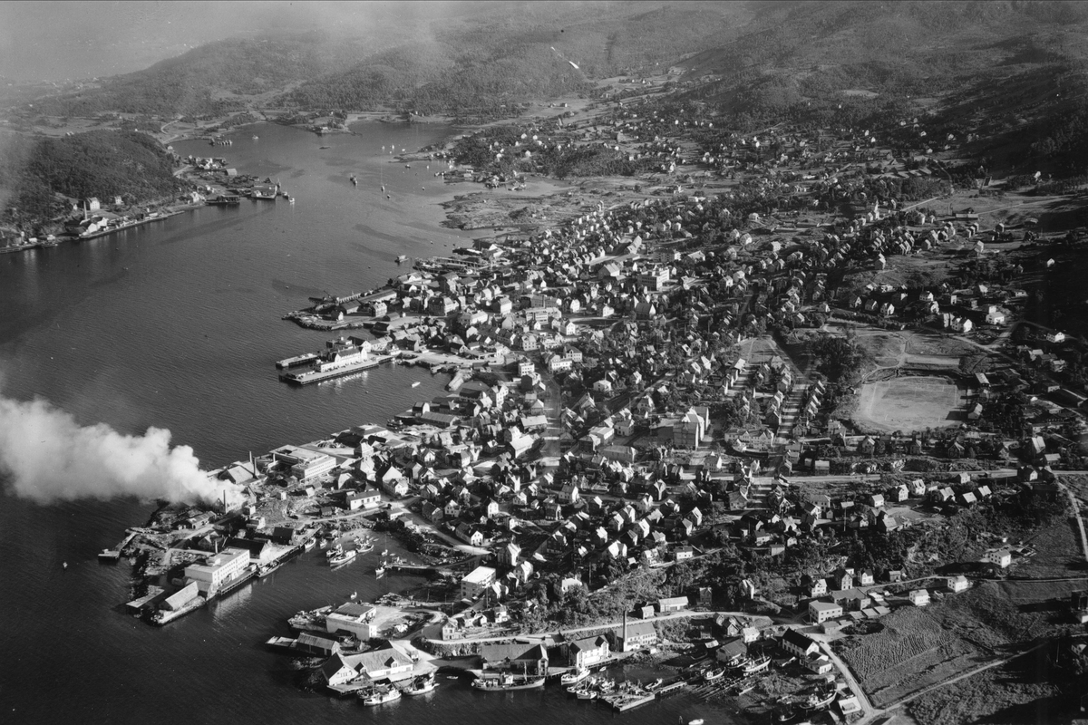 Flyfoto av Harstad by. Brannrøyk fra Hamnneset. Strandgata midt i bildet, Harstad stadion til høyre.