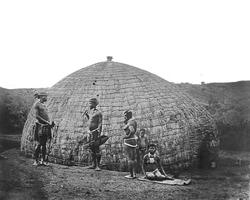 Innfødte ved sine hytter, Sør-Afrika