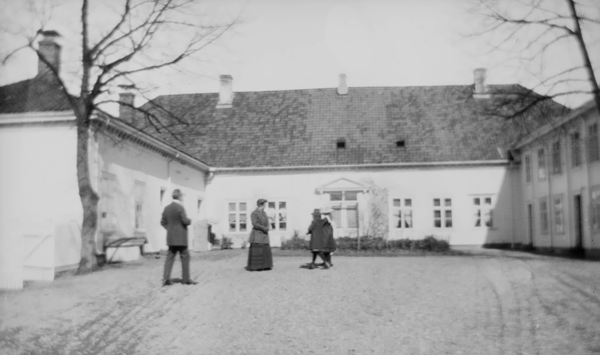En kvinne og en mann samt to barn oppholder seg på gårdsplassen utenfor et hesteskoformet hus.
