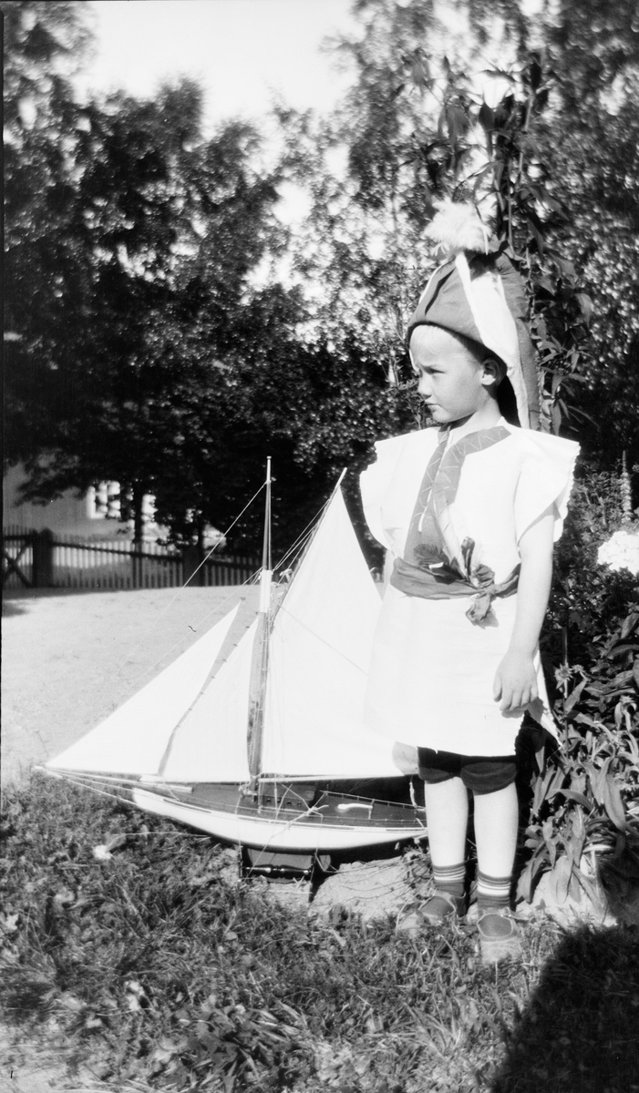 Iacob Ihlen Mathiesen står i hagen, utkledd som kaptein og med en lekeseilbåt stående ved siden av seg.