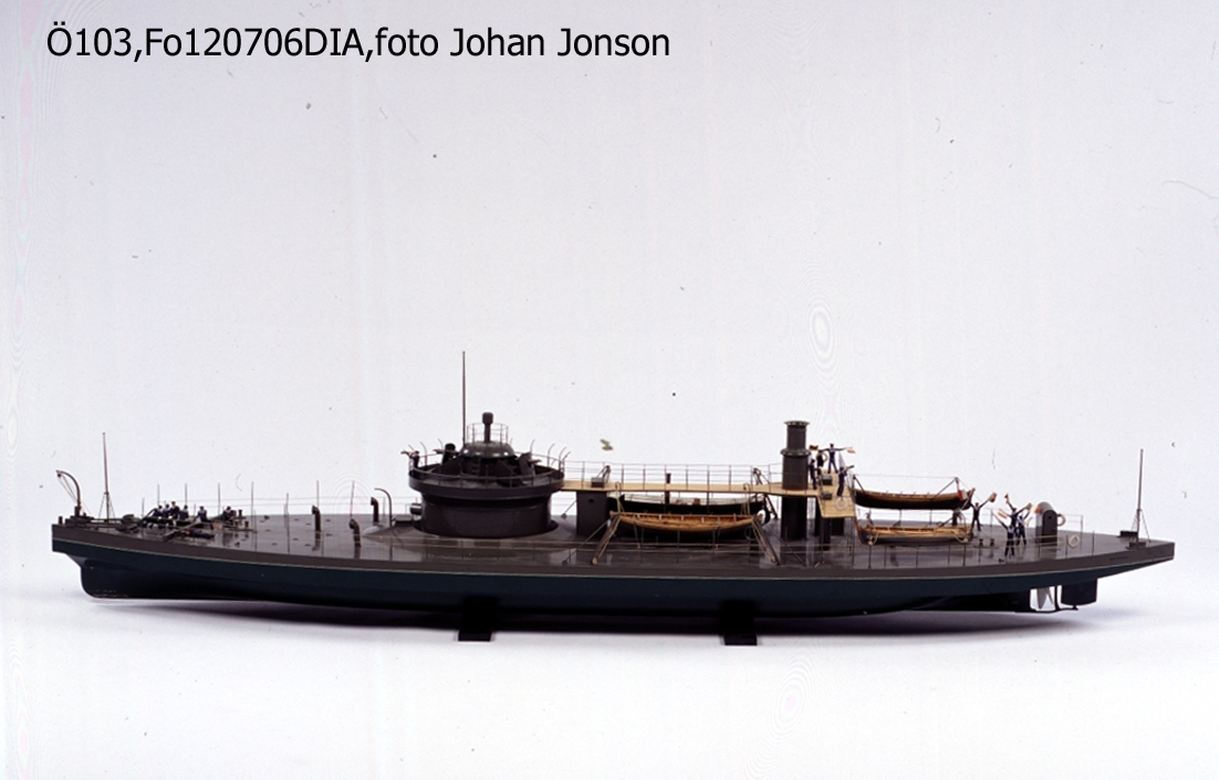 Fartygsmodell, 2:a klass pansarbåt John Ericsson. 

Byggd i block med fullständig däcksinredning, roder, vitmålad propeller, gös- och vimpelstake, flaggspel, flagga, gös och vimpel. Gråmålad, vattengång grön med svart botten. Vit vattenlinje.  2 kanoner 2 kulsprutor av järn, omålade. Ångslup i dävertar och skrå. Slup, låringsbåt och jolle, byggda på spant, klink, fullständigt inredda med respektive 4, 4 och 2 stycken åror, i dävertar. Stativ: 2 metallstöttor.