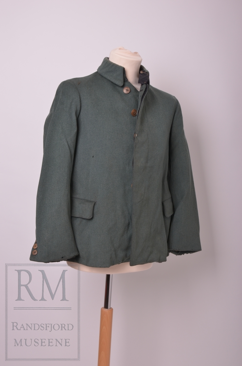 Mørk grønn jakke med svak A-fasong. Skjult knappestolpe og høy krave med korte snipper. Ikke originale knapper.