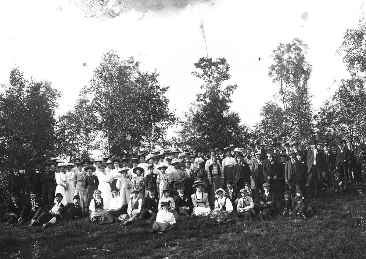 Gruppbild av ett otal kvinnor och män fotograferade utomhus. Samma motiv som neg.nr. B403.