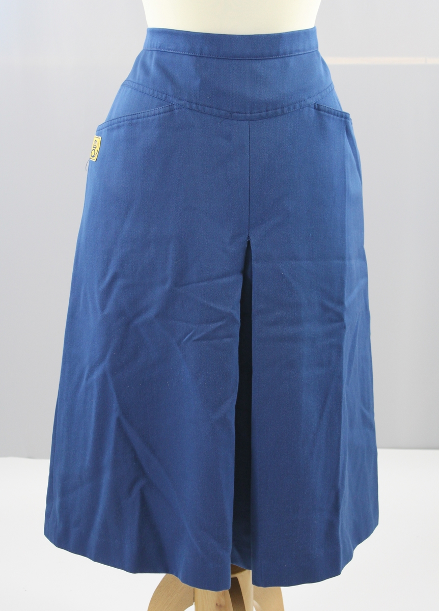 Kjol i blått med veck framtill två sidfickor och svart foder. Blixtlås i ryggen och en postsymbol vid den högra sidfickan.