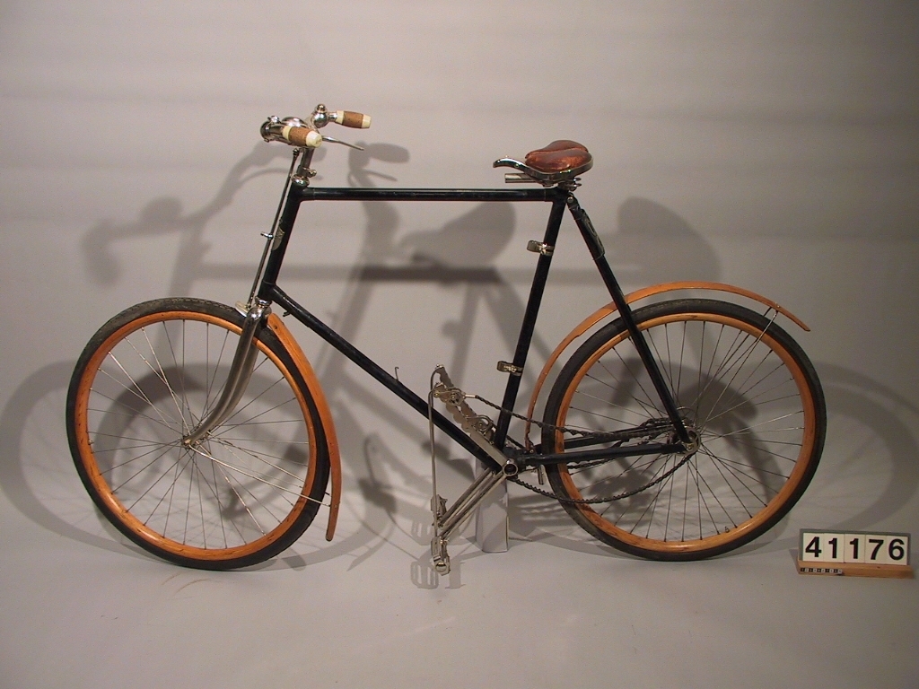 Cykel av Svea-typ. Ram av stålrör, med skärmar och fälgar av trä, handtagen är av kork, sadeln består av läderklädd förnicklad plåt. Sammansatt av delar från flera cyklar.