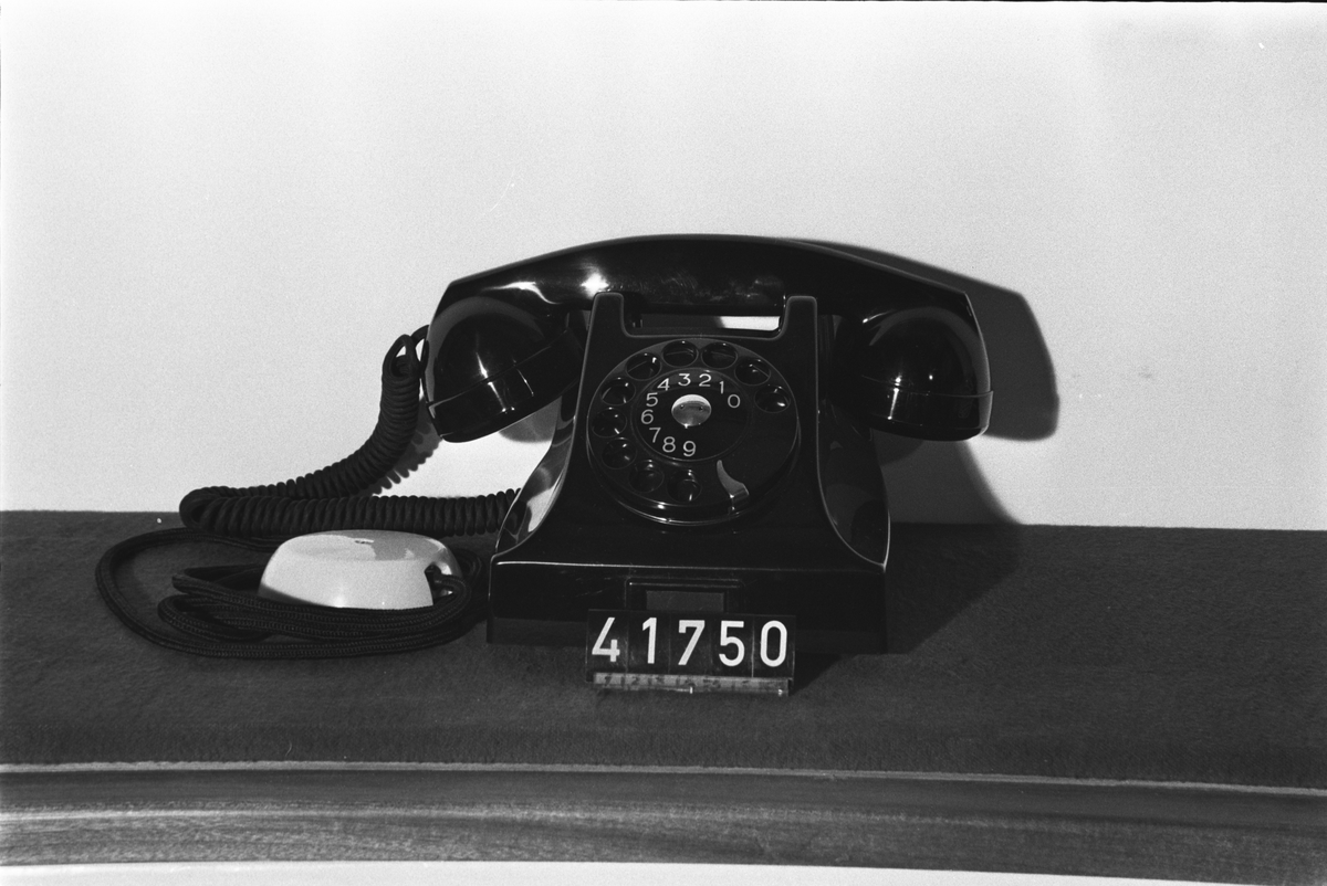 Telefonapparat BC 560, ändstationsapparat för AT-system. Bordapparat modell m50 av svart bakelit med apparatsnöre anslutet till väggplint med lock av vit plast.