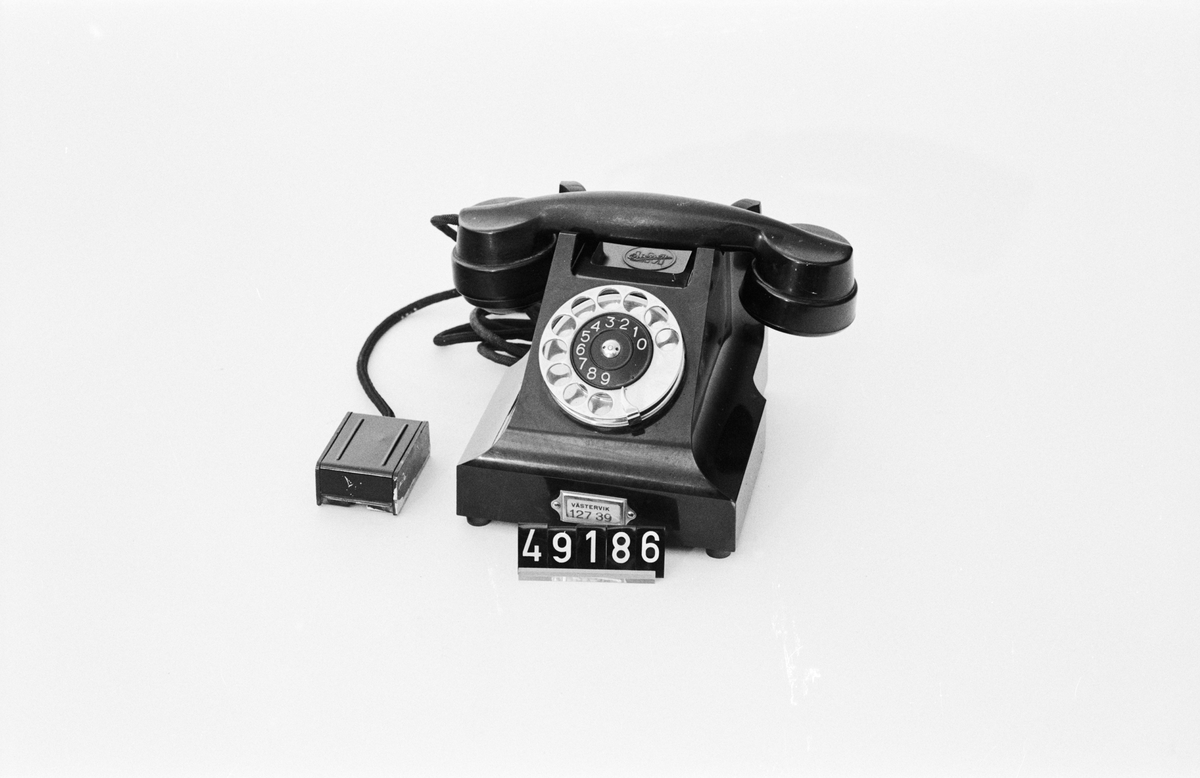 Telefonapparat BC 330, ändstationsapparat för AT-system. Bordapparat modell m33 av svart bakelit med fingerskiva av förnicklad mässing och textilklätt apparatsnöre anslutet til väggplint med lock av svartlackerad plåt.