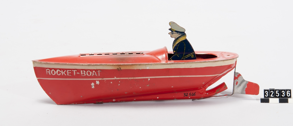Tillverkad av rödmålad plåt. Leksaksbåten drivs med en Metatablett som vid påtändning värmer luft som via ett rör i aktern driver båten framåt.