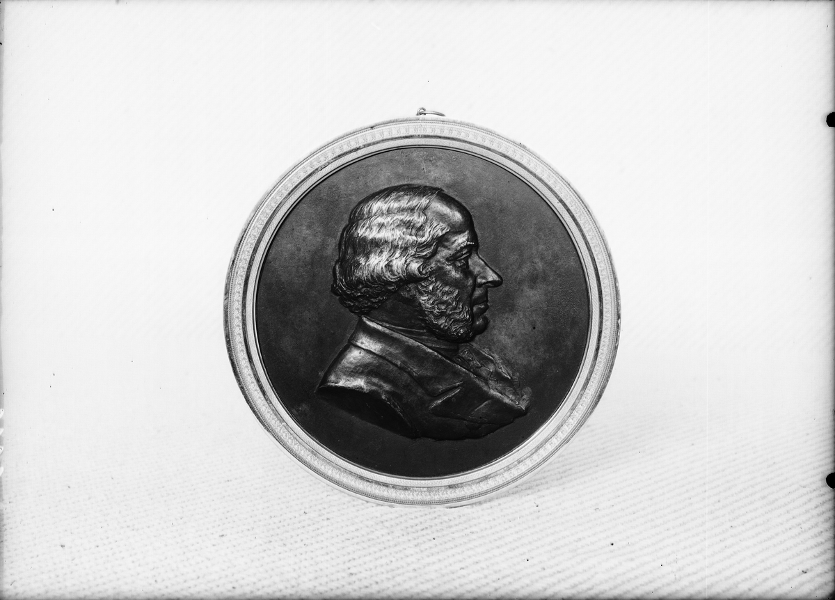 Medaljong gjuten i brons, över John Ericsson. Med ram av brännförgylld mässing.