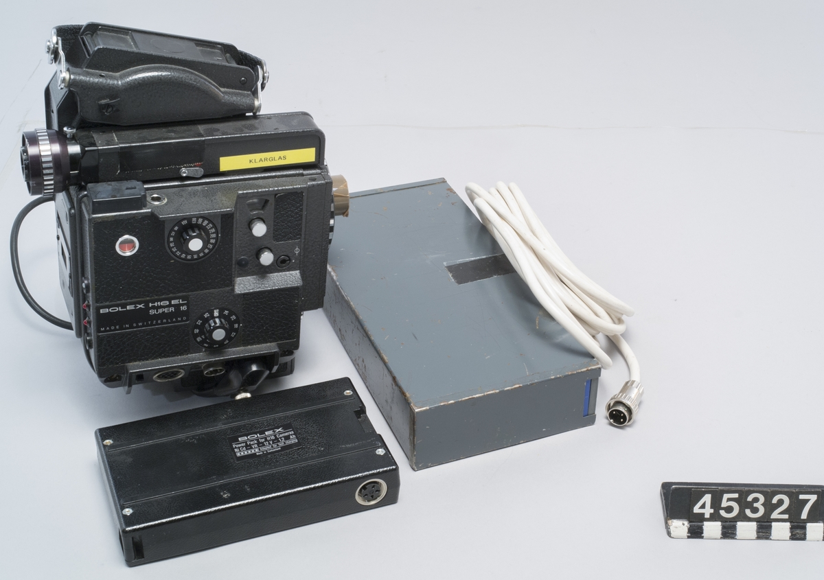 Filmkamera Bolex typ H16 EL för eldrift. Format Super16, anpassad för filmning via mikroskop. Med två batterier: ett i grå plåt, och ett i plast samt en batterikabel.