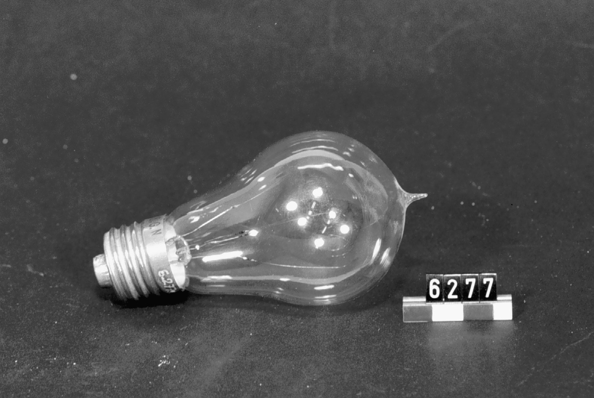 Elektrisk koltrådslampa med två glödtrådar, normalfattning, päronform, 220 volt, 16 n. ljus. Märkt på fattningen:"S.G.N. 220 16". Glödtråd av kolad cellulosa.