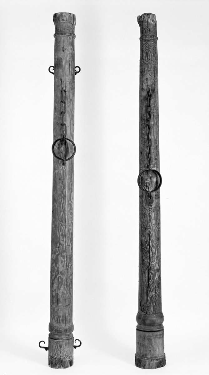 Brune trestokk med enkel utskåret profilering i form av runde bånd øverst og nedert. Påmontert halsjern med lenke og hengelås.