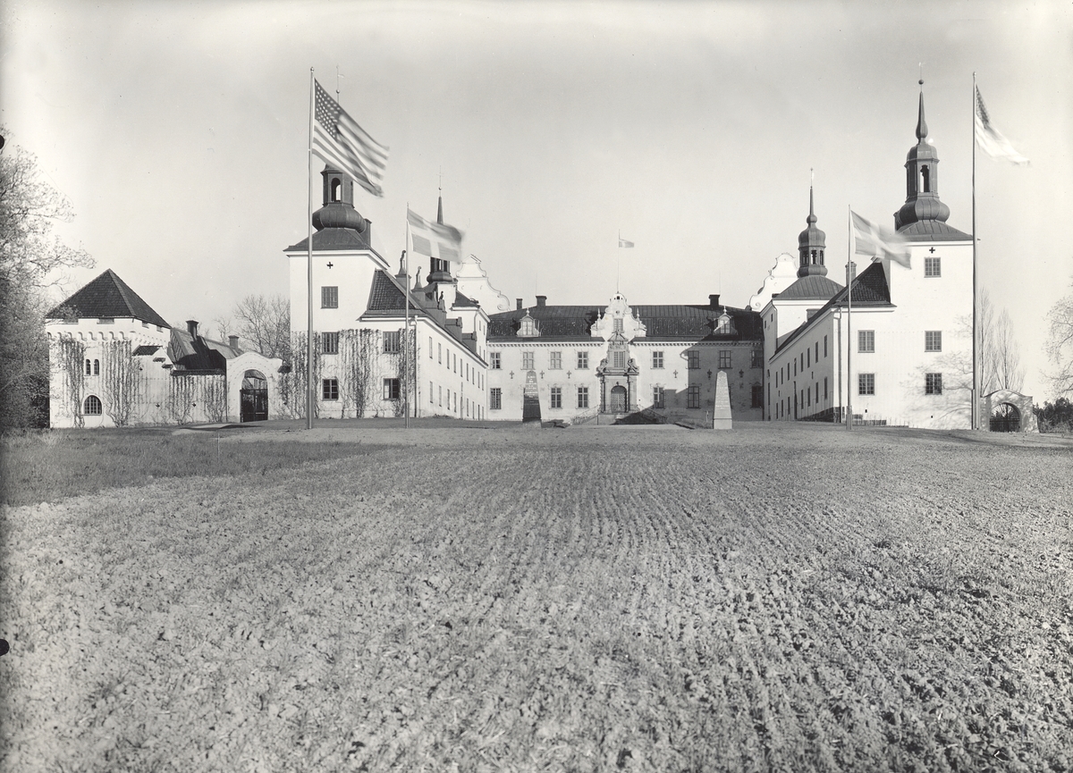 Tyresö slott från entrésidan. Gårdsplanen är krattad och framför byggnaderna vajar svenska och amerikanska flaggor.