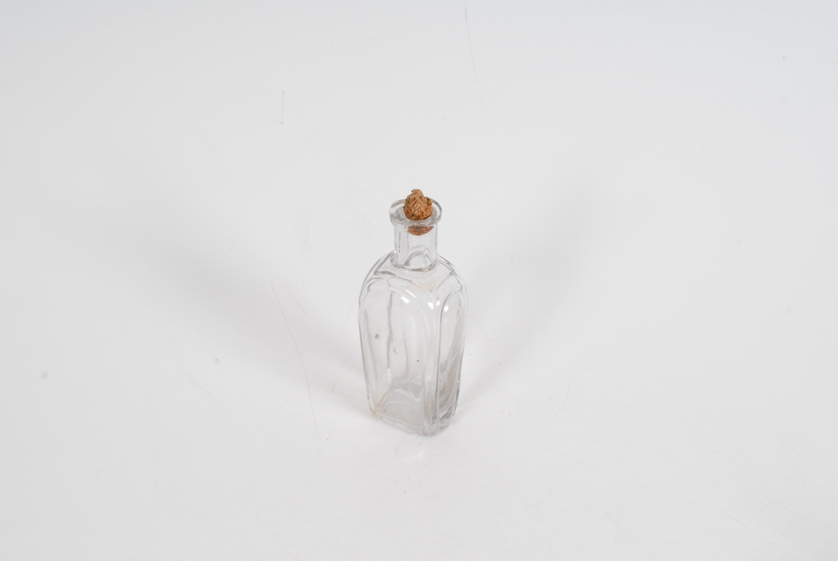 Gglasset er bueformet ved flaskens hjørner/kanter og i bunnen er det et enkelt blomsterlignende motiv. 