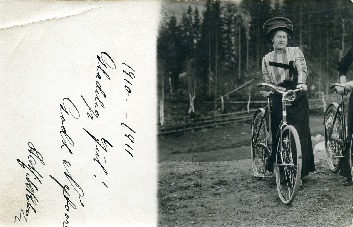 Prospektkort av Anna Bergsund som står ved en sykkel. Tatt ca. 1910.