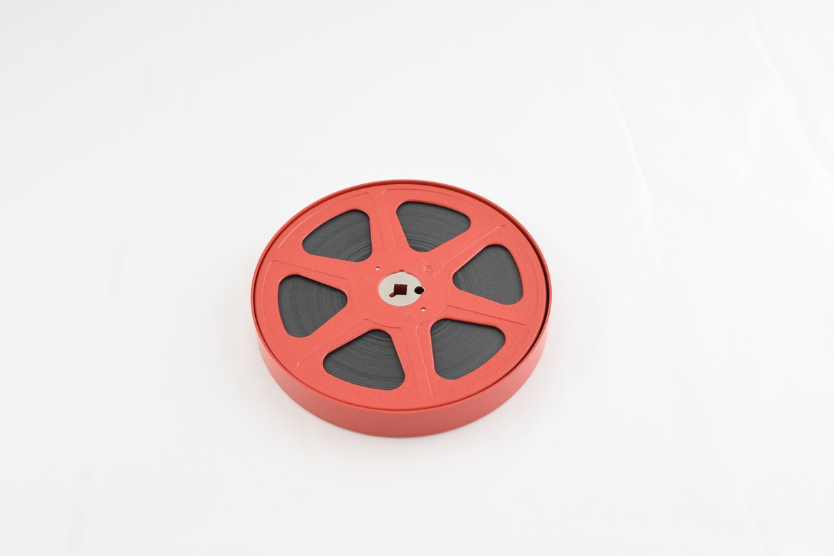 Filmrull i eske. Film på rød plastikkspole. Rødt rundt etui med rund grønn etikett.