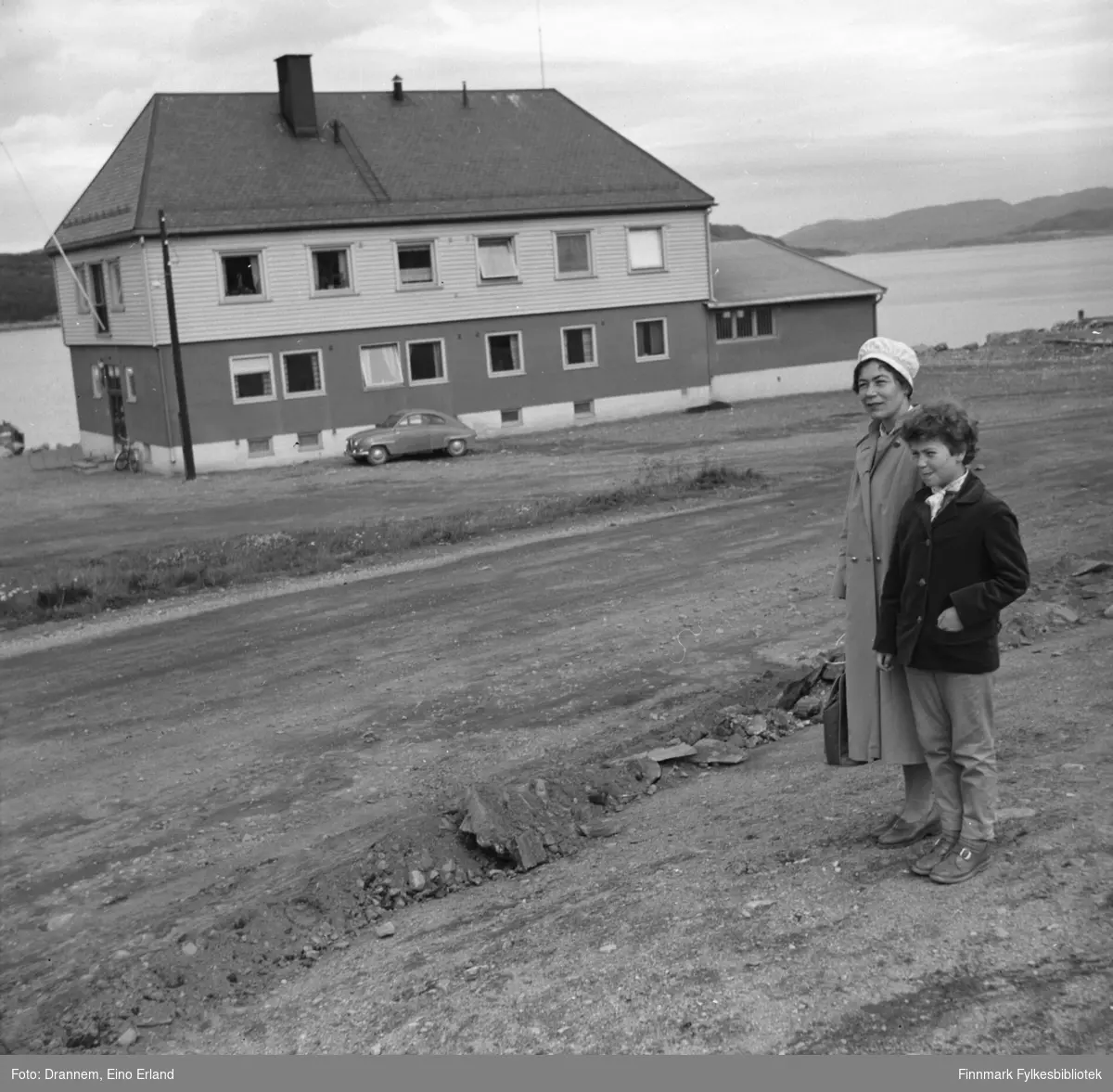 Fotografi av Jenny Drannem og Turid Karikoski et stykke foran en stor bygning, "Tollbygget" i Kirkenes
