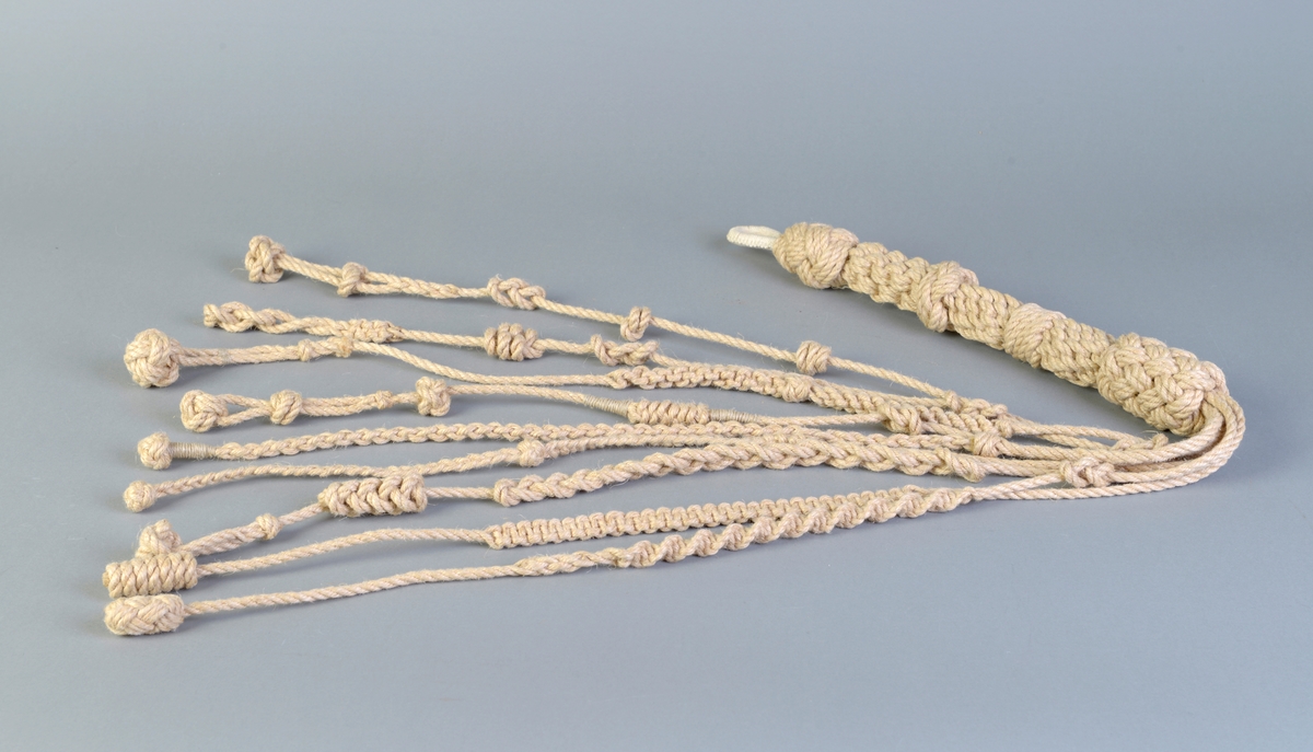 En piskeanretning av hampetau utformet med et knytt håndtak hvor det utgår ni taulengder fra med ulike knuter i forskjellig former på.