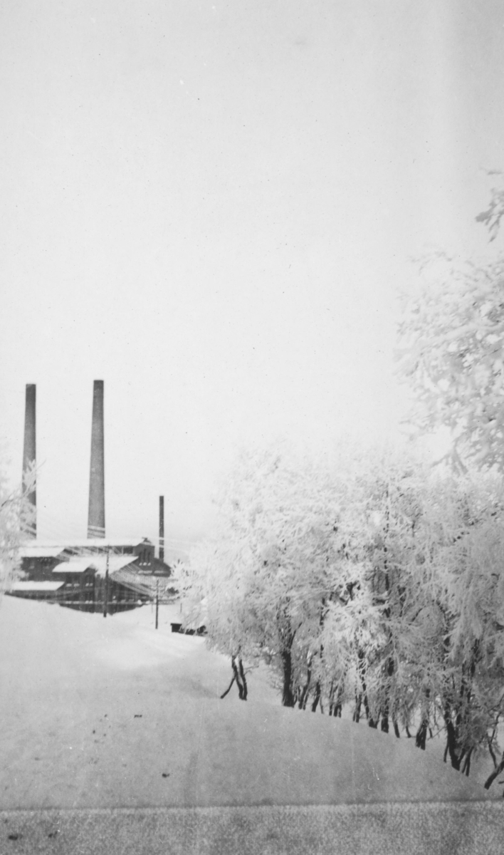 'Fra Kirkenes (fra doktorgaarden nedover).' Vi ser deler av A/S Sydvaranger til venstre, som ble stiftet i 1906. Det er vinter og snø.