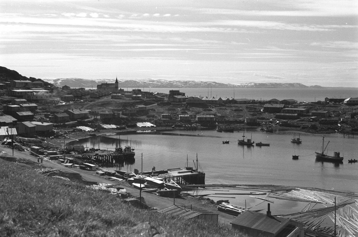 Gjenreisning. Honningsvåg. Brakkebebyggelse rundt Vågen. Tømmer i sjøen. I bakgrunnen Honningsvåg kirke. 1946/47.