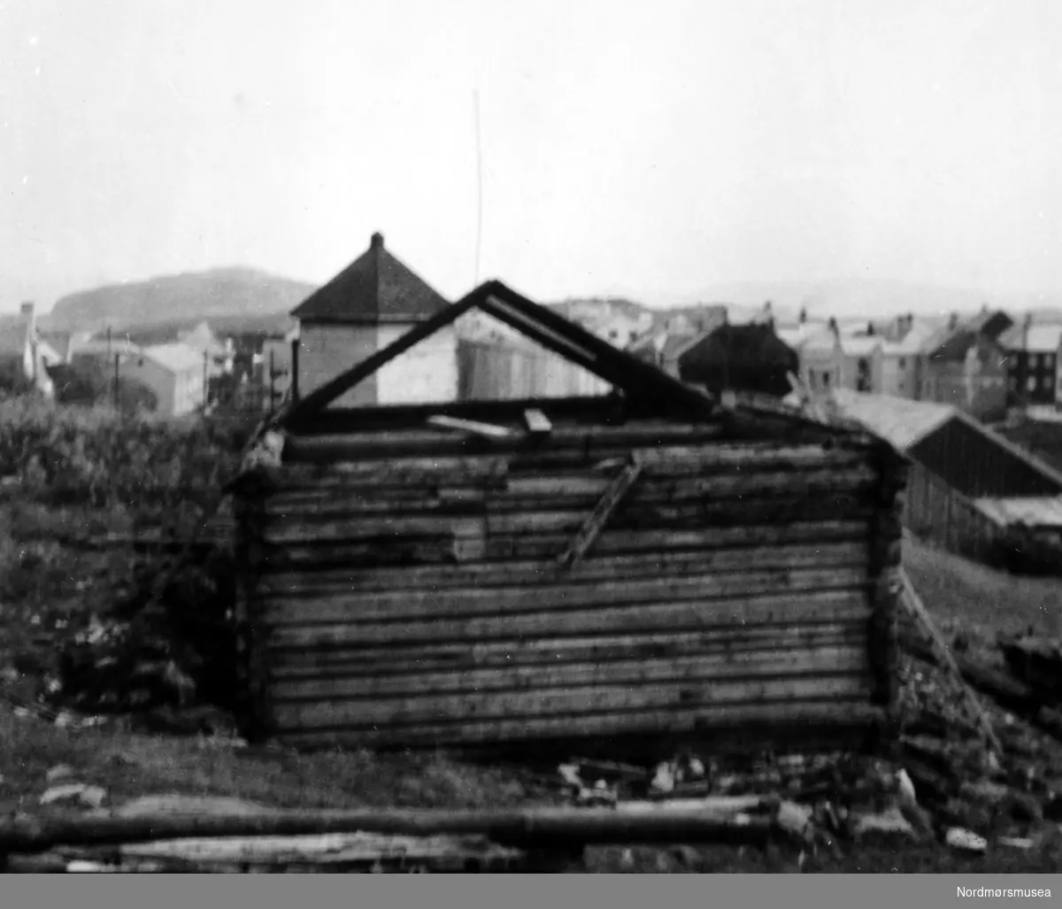 Almskårstua rives i Clausenengen, og taksperrene med nederdelen av stua står igjen. I bakgrunnen ser vi Vardetårnet. Bildet er datert 11. juni 1958. Serie. Nordmøre Museum