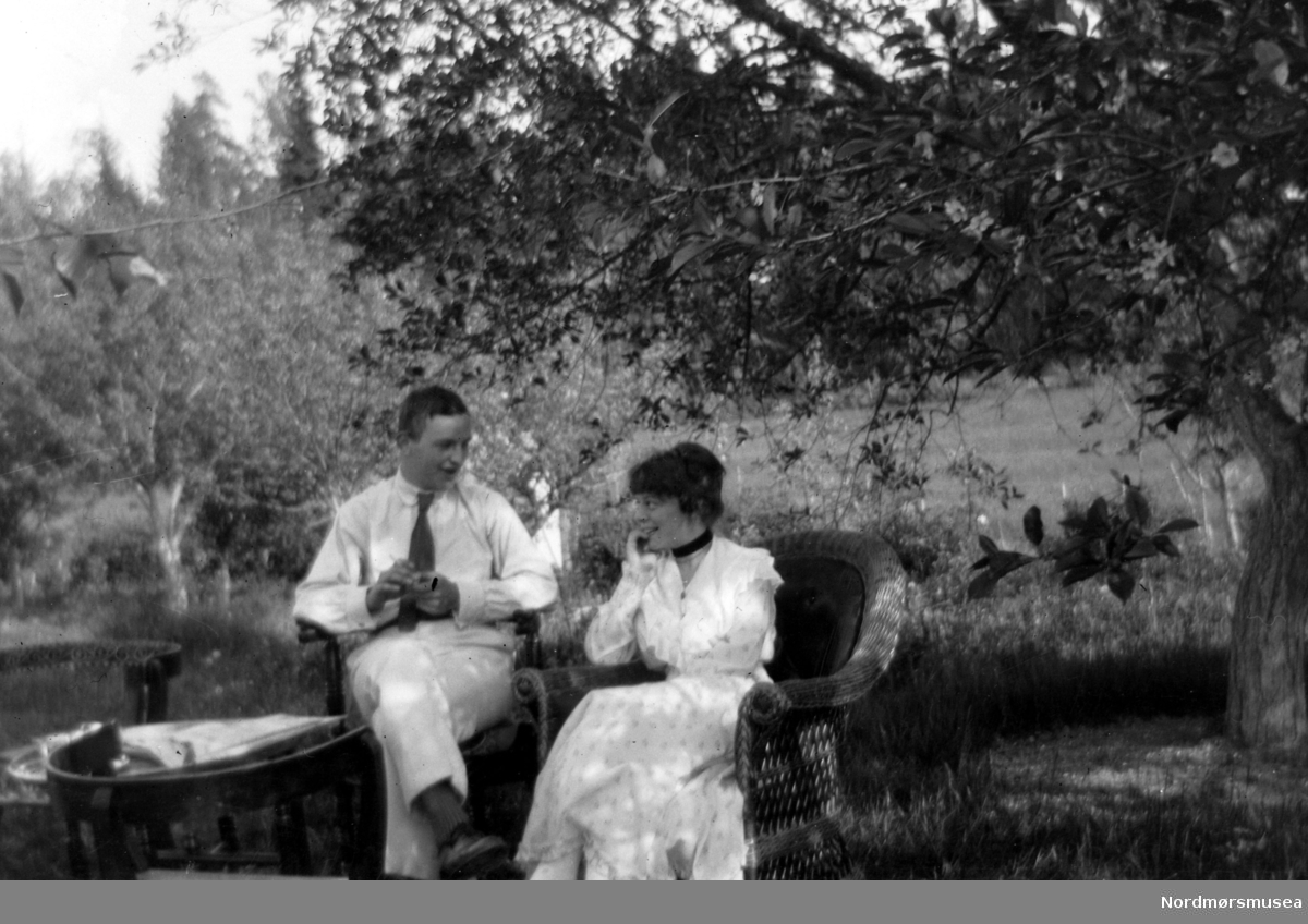 Foto av en mann og kvinne sittende ute i en hage og nyter sommeren. Mannen på bildet er en av sønnene til Margrethe og Georg Sverdrup, den unge damen er ukljent.Sted og datering er også usikkert, men kan trolig tidfestes til omkring 1915 ti 1925, og da i Møre og Romsdal fylke. Fra Nordmøre museums fotosamlinger.
