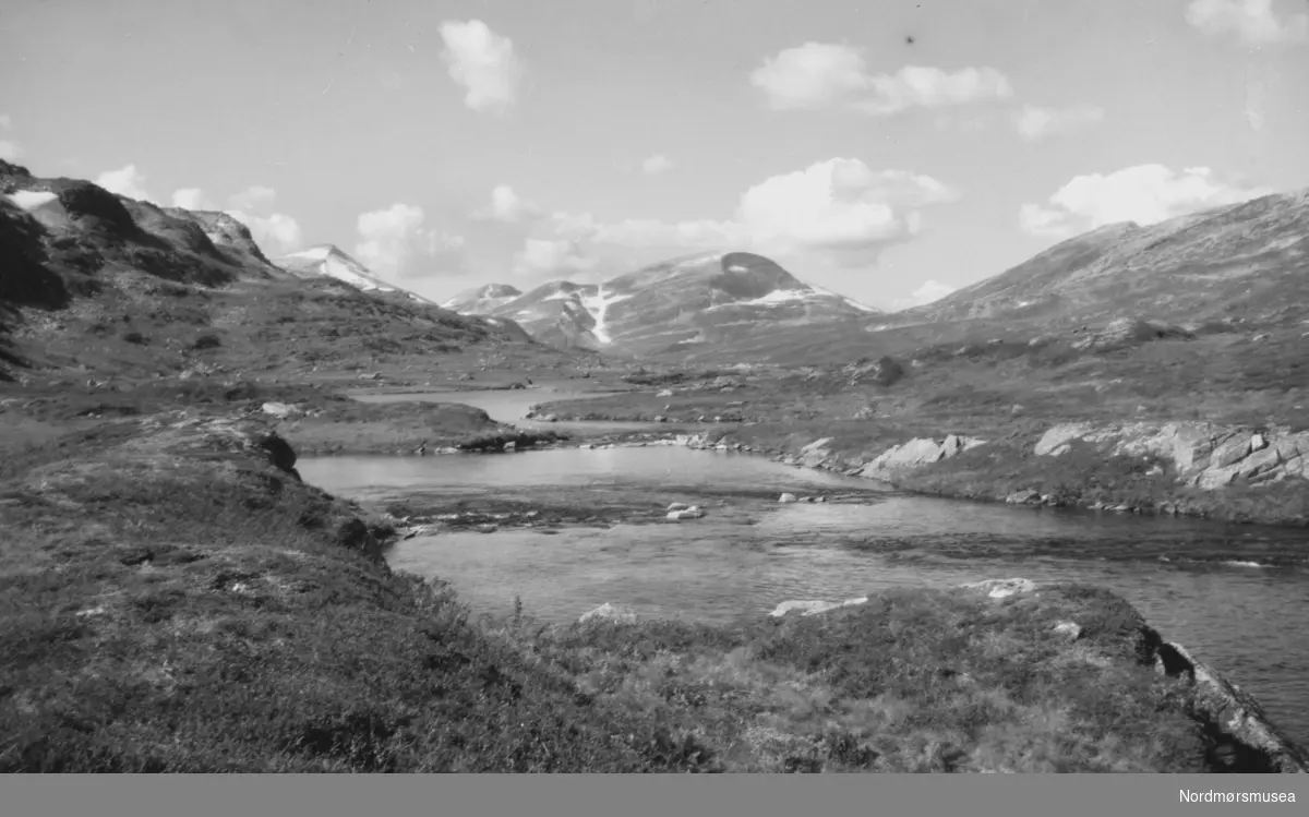 Landskapsbilde
fra
en elv i forgrunnen og
med store fjell i bakgrunnen. Trolig
i Sunndal kommune. Datering er ikke kjent, men kan muligens være fra tiden omkring 1930 til 1960. Fra Nordmøre museums fotosamlinger.
