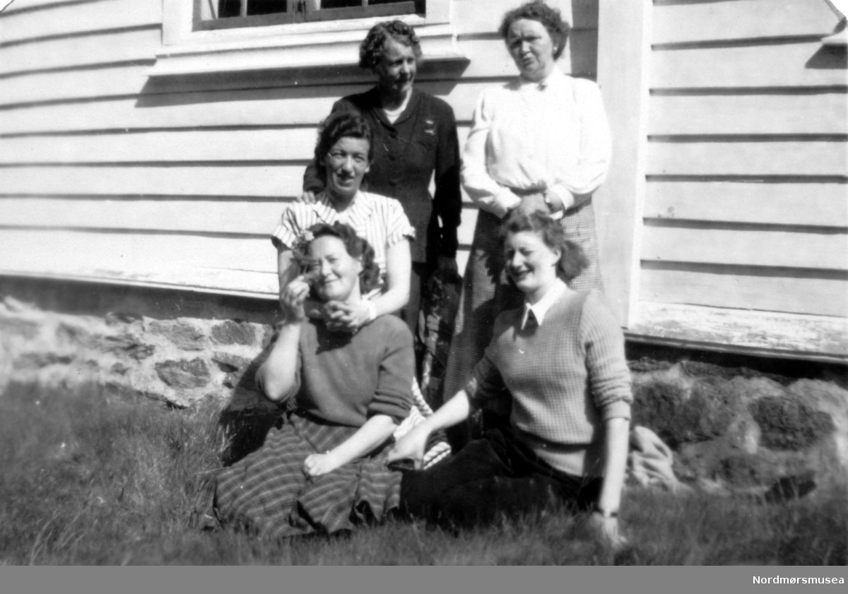 Foto av en gruppe kvinner på tur, her er noen samlet utenfor en bolig. Bildet kommer fra en samling foto av kvinner tilhørende ";APs Kvinneforening 1960";. Det er ukjent hvem vi ser på bildet. Fra Nordmøre Museums fotosamlinger.
