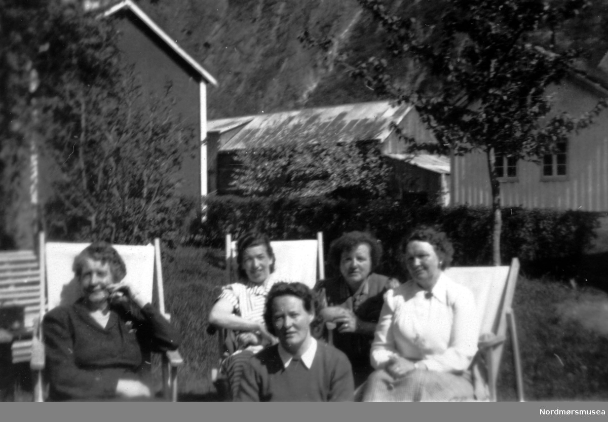 Foto av en gruppe kvinner sittende i noen hagestoler. Bildet kommer fra en samling foto av kvinner tilhørende ";APs Kvinneforening 1960";. Det er ukjent hvem vi ser på bildet. Fra Nordmøre Museums fotosamlinger.
