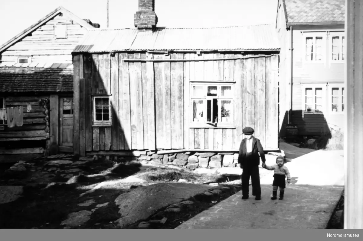 fiskeværet Grip utenfor Kristiansund. Håja (eller Haugen) på Grip. Huset bak til høyre, bygd 1915-1920,  ble revet omkring 1948.
(Info: Paul Bakkmyr 2018).  klesvask, blikktak, laft, betongvei, barn. ca 1925. Fra Nordmøre museums fotosamlinger.