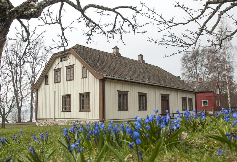 Hvitt hus med valmet tak og blå blomster i forgrunnen. (Foto/Photo)