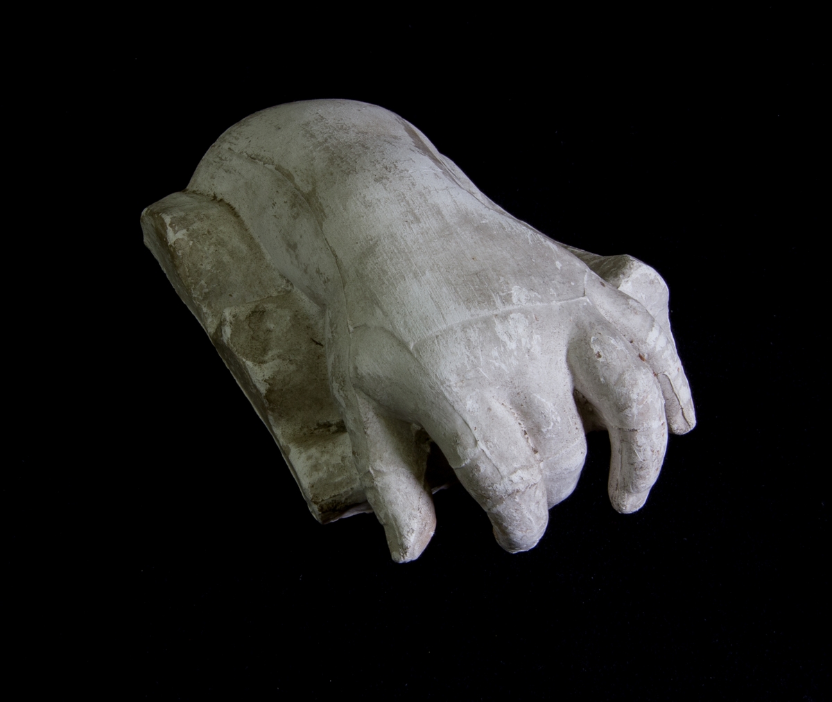 Studie av gips föreställande en hand och delar av armen som vilar på ett svängt underlag. Ögla för upphängning.